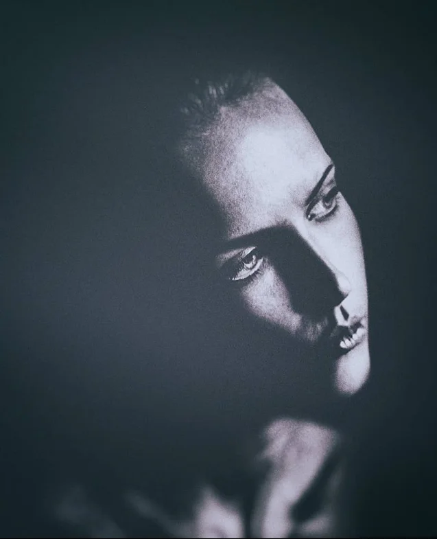 Black and white fine art portrait of a woman in dramatic shadow